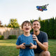 Boy flying the blue remote control foam fighter jet in the yard with his father