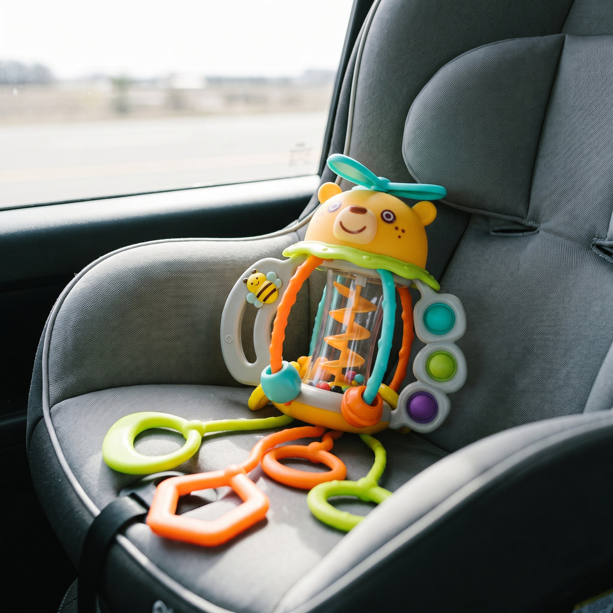 The bear rattle lying on an empty grey car seat, its teething rings spread across the padding