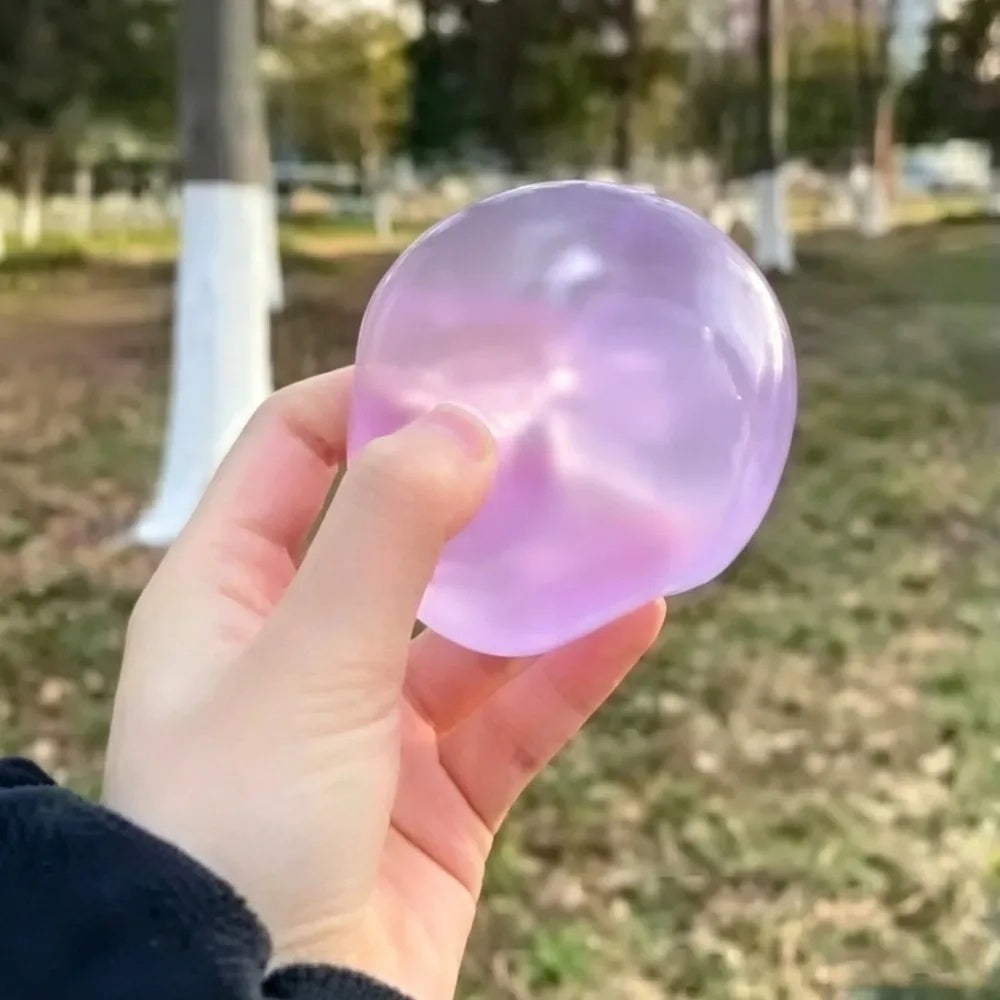 Purple coconut oil squishy ball squeezed in a hand outdoors