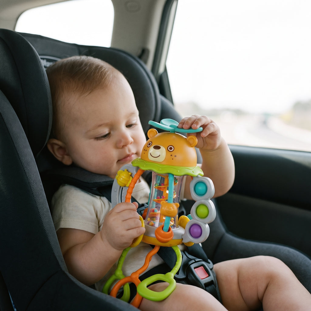 Baby strapped in a car seat, holding the bear rattle against their chest and spinning the turquoise propeller on top of the bear's head