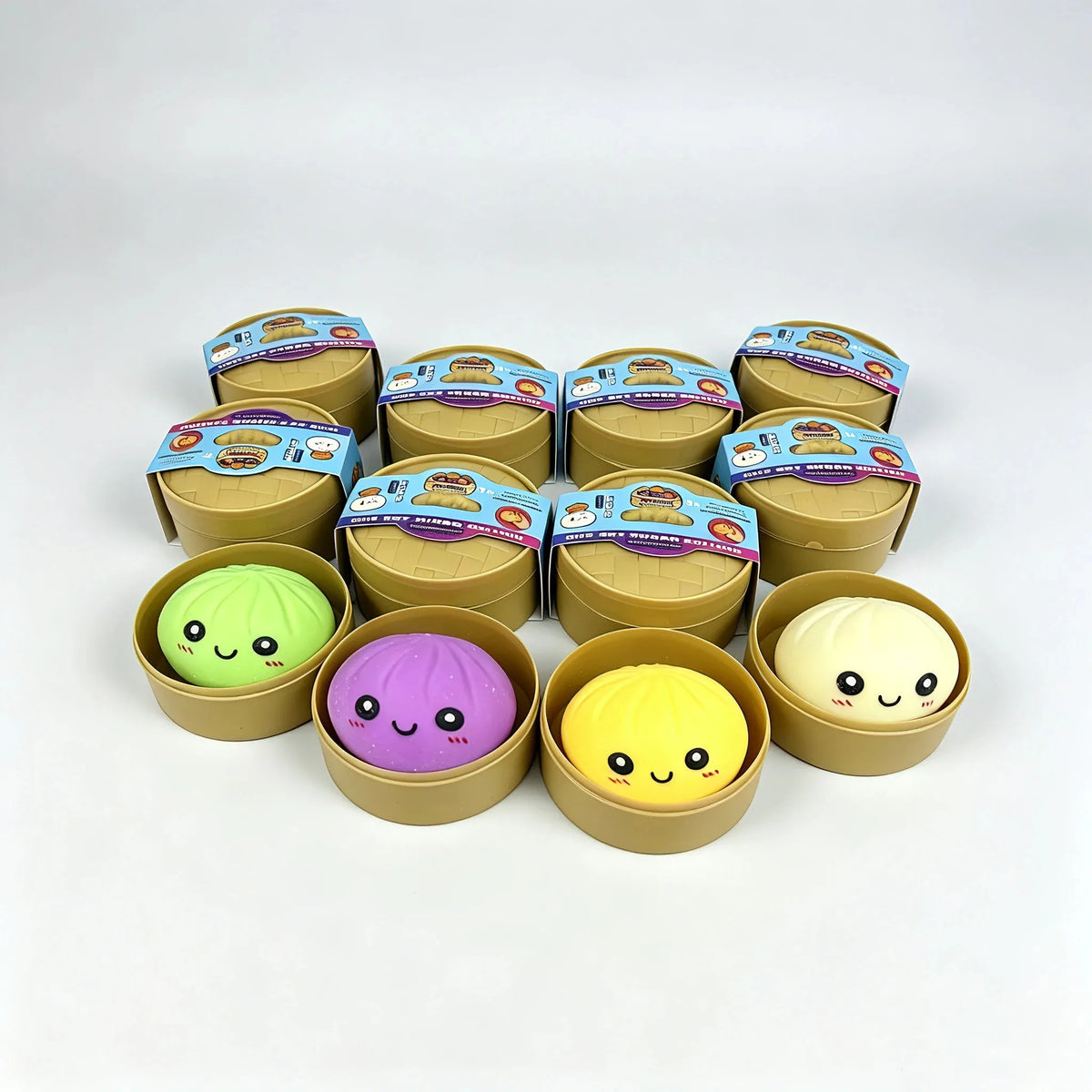 The four dumpling squishy designs in their steamer baskets, purple glitter, green, yellow and cream, with sealed blind boxes behind