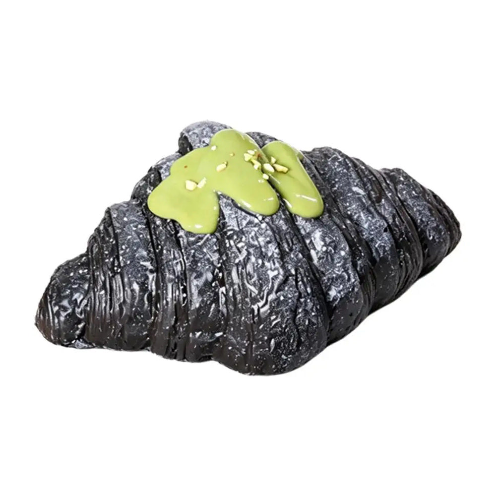 Black croissant squishy toy with green topping on a white background