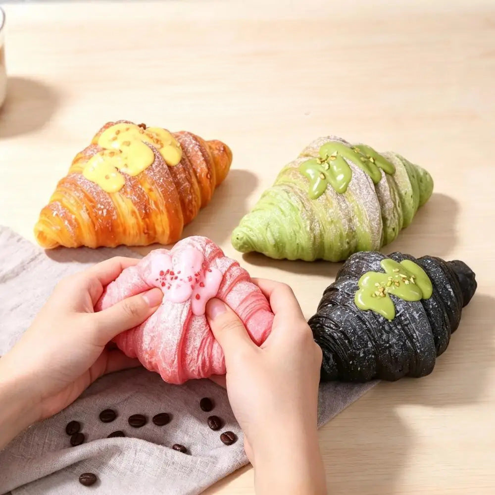 Hands squeezing a pink croissant squishy next to golden, green and black ones