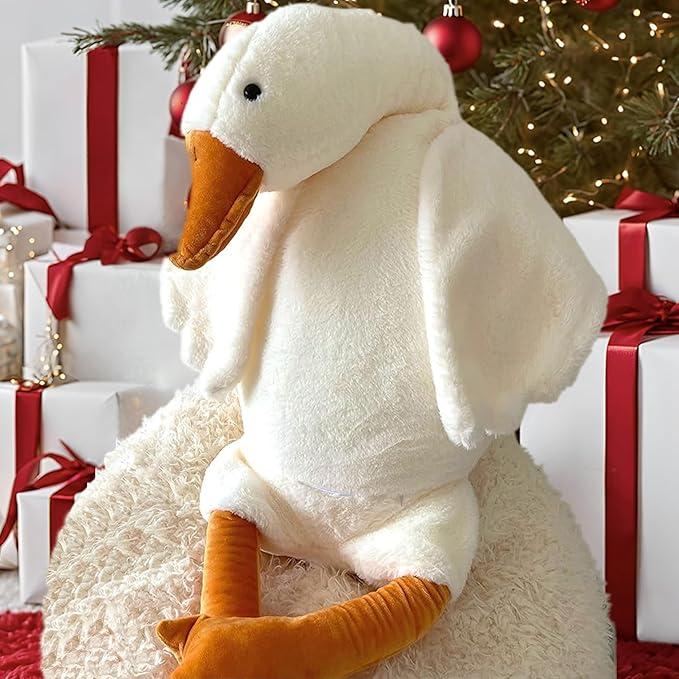 White goose plush sitting in front of a Christmas tree and wrapped gifts