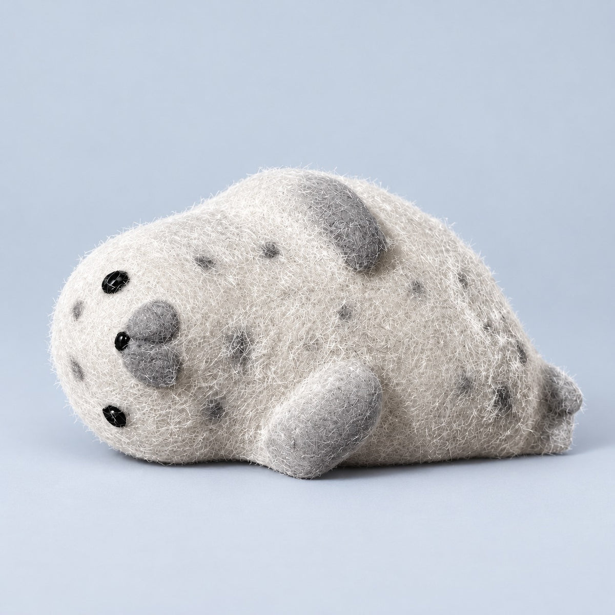Grey spotted fuzzy seal squishy lying on a plain pale blue background