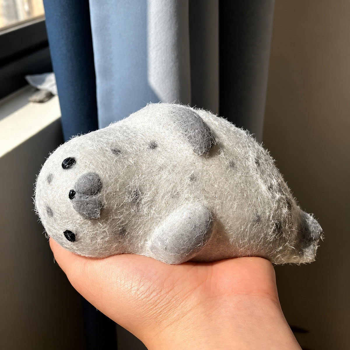 Grey spotted fuzzy seal squishy lying in an open hand by a sunny window