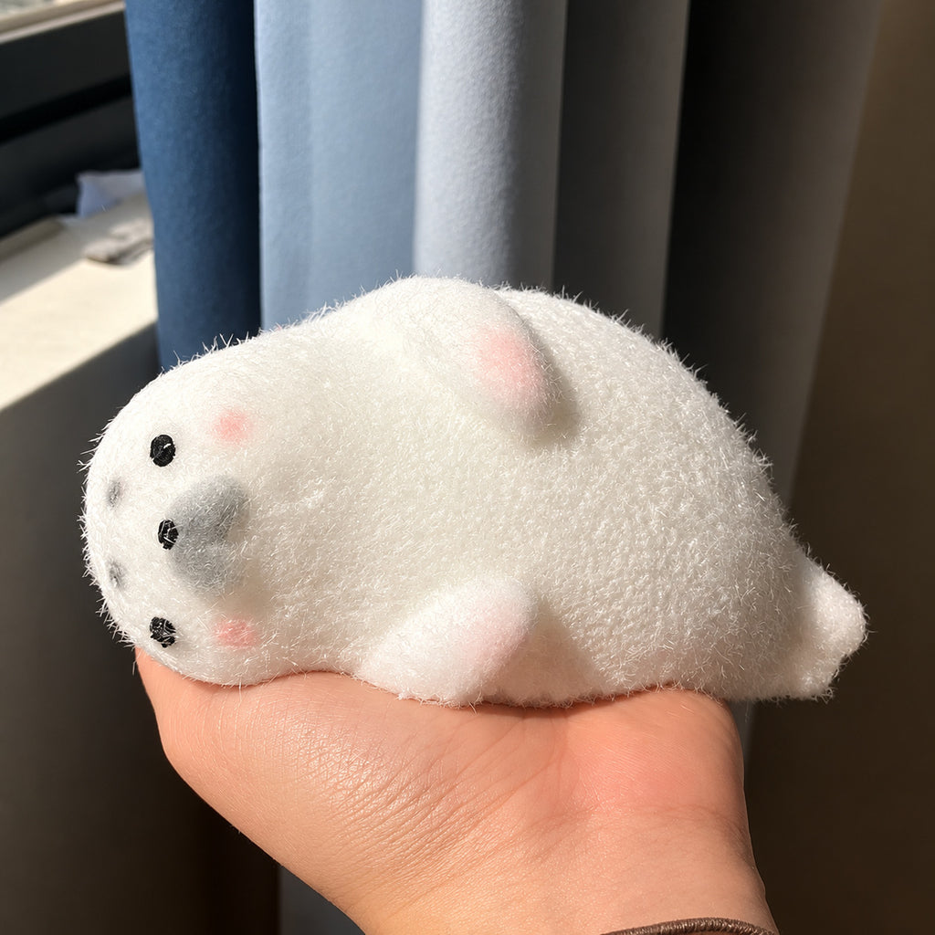 White fuzzy seal squishy with pink cheeks lying in an open hand