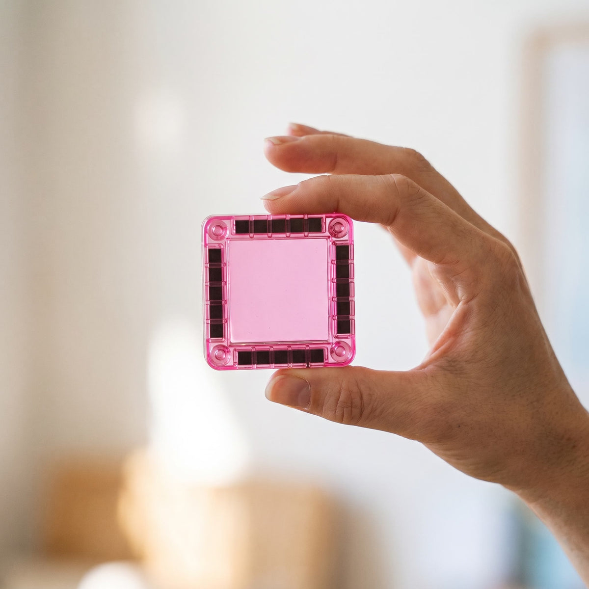 Adult hand holding one 3.75 cm pink magnetic tile between finger and thumb to show its size