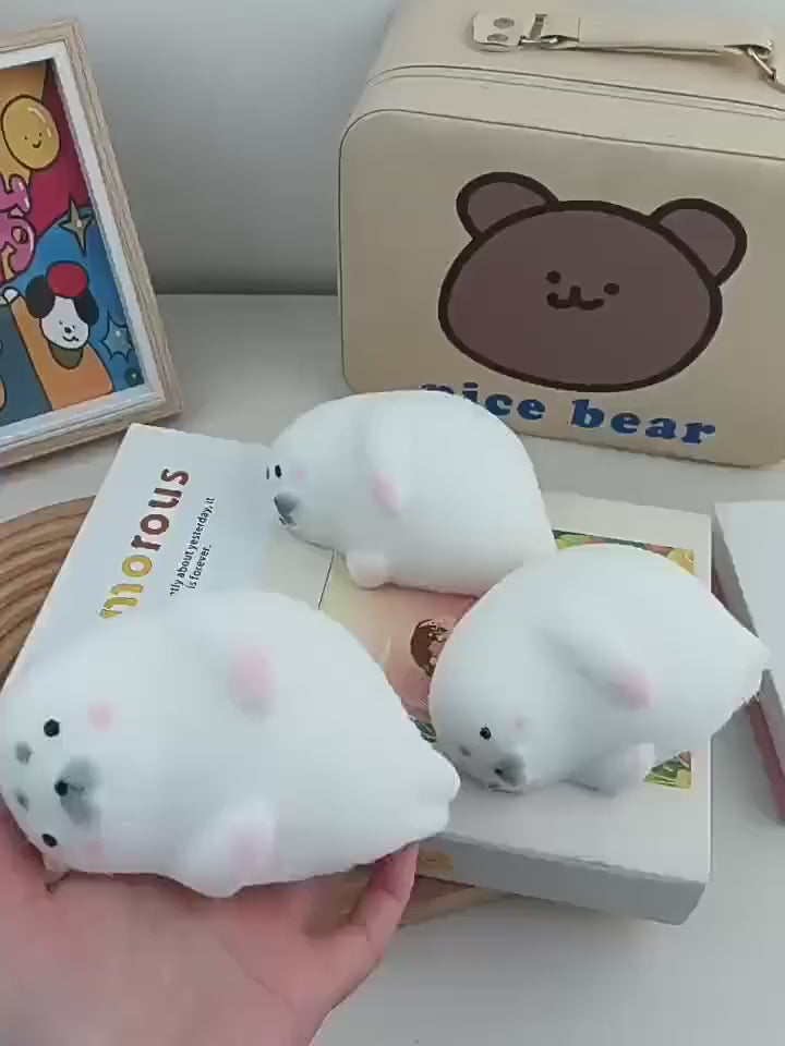 Hands squeezing the white fuzzy seal squishy, which puffs back into shape