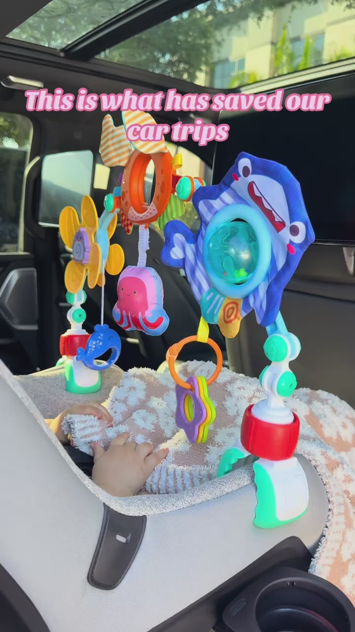 Play arch clipped to a car seat handle keeping a baby calm on a car ride