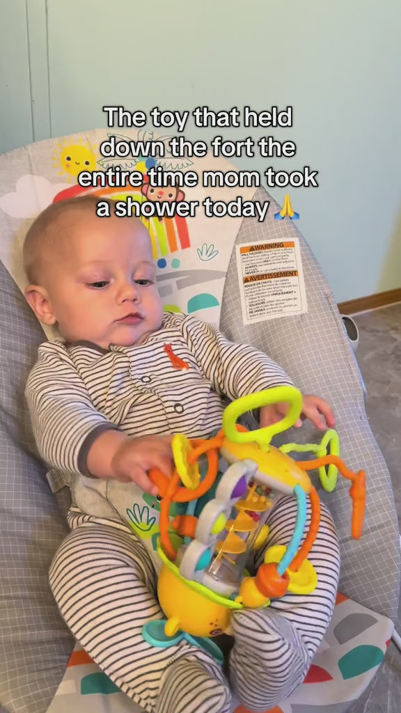 Baby lying in a bouncer holding the bear rattle and mouthing one of its silicone rings