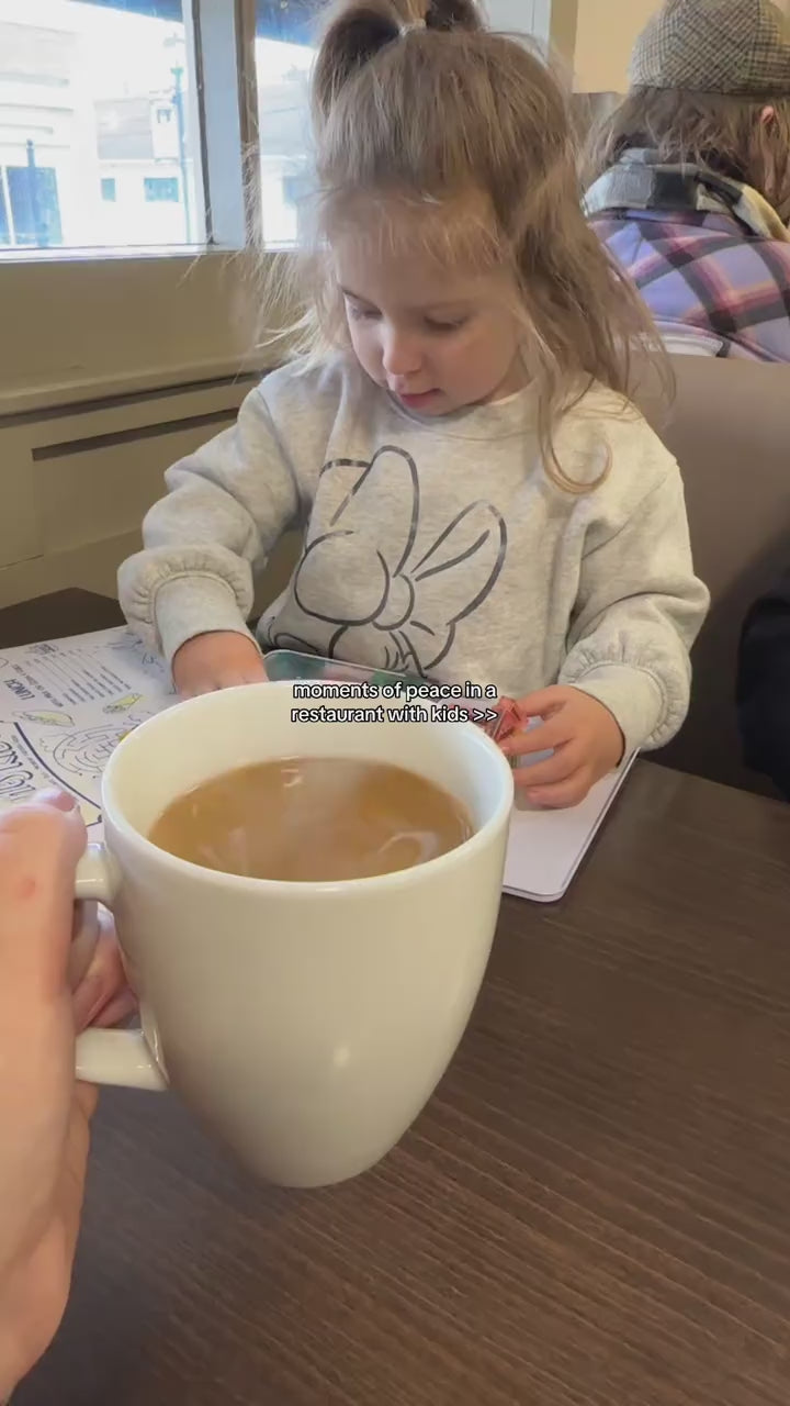 Toddler building with mini magnetic tiles at a restaurant table while her mother drinks a hot coffee