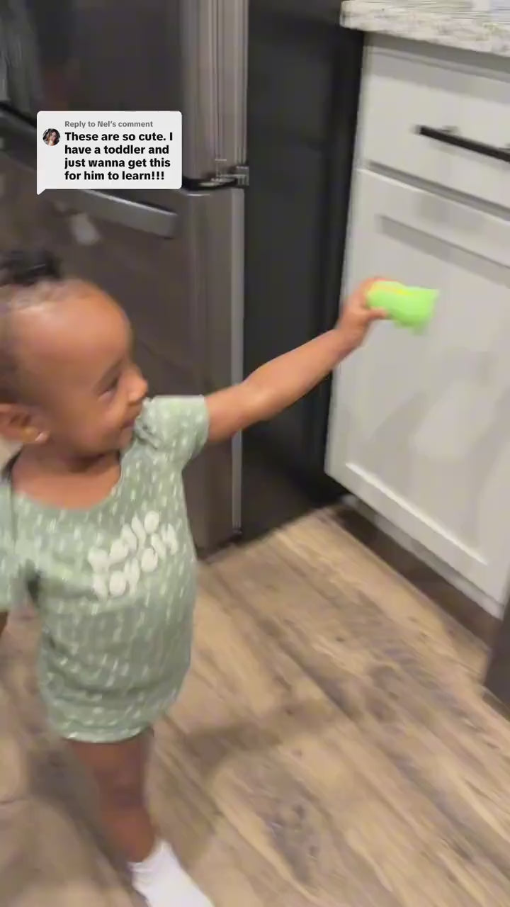 A toddler carries the dinosaur reader across the kitchen, sets him on a sticker on the fridge and on the oven, and hears the word each time
