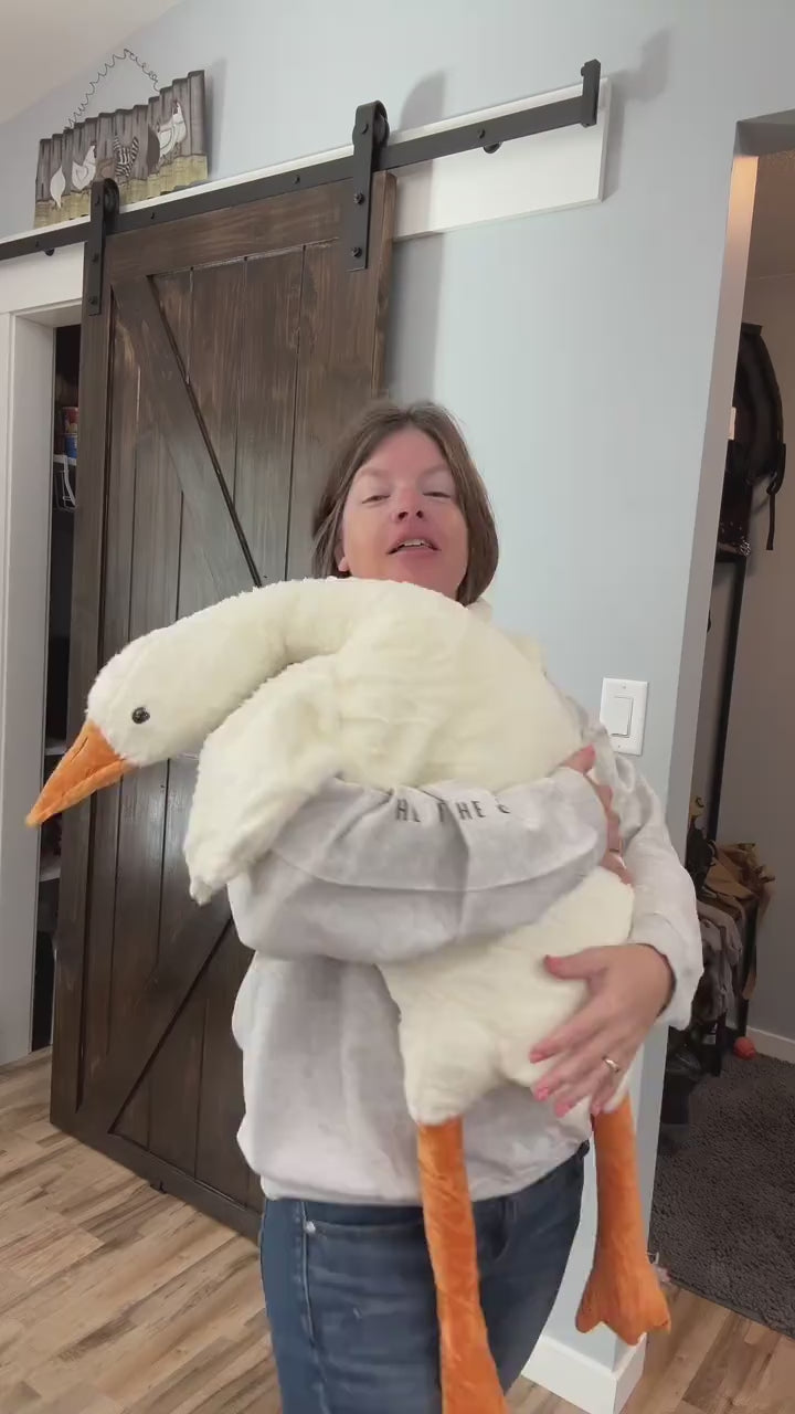 A woman holds the goose plush up to show how tall it is next to her