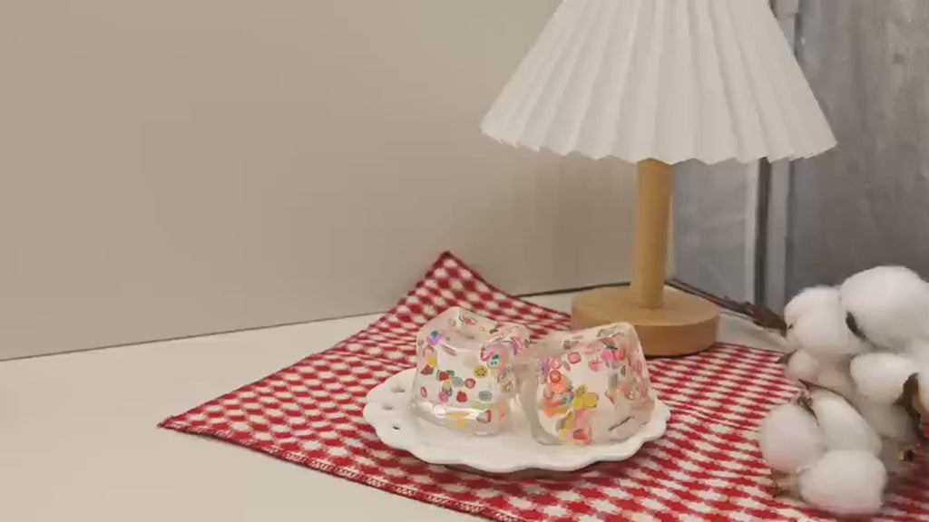 Hands squeezing and stretching the clear fruit ice cube squishy, which goes back to a cube