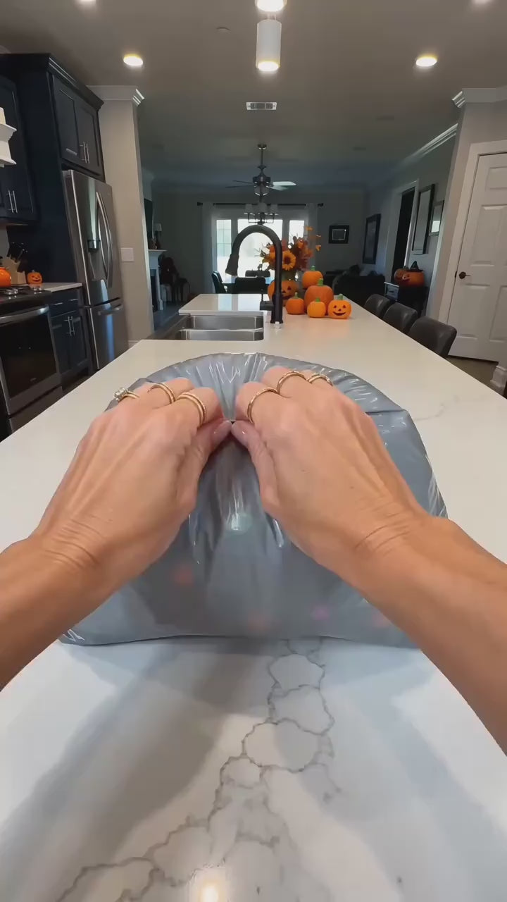 Halloween mochi squishies poured out of a plain mailer onto a kitchen counter, each piece sealed in its own clear bag, then a white ghost and an orange pumpkin held up to camera