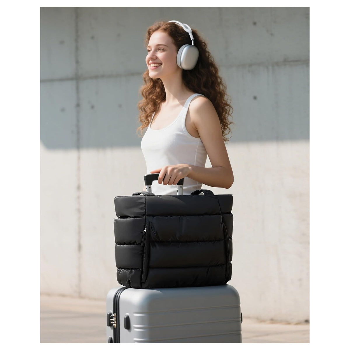 Woman walking through the airport with the black puffer tote resting on her suitcase handle