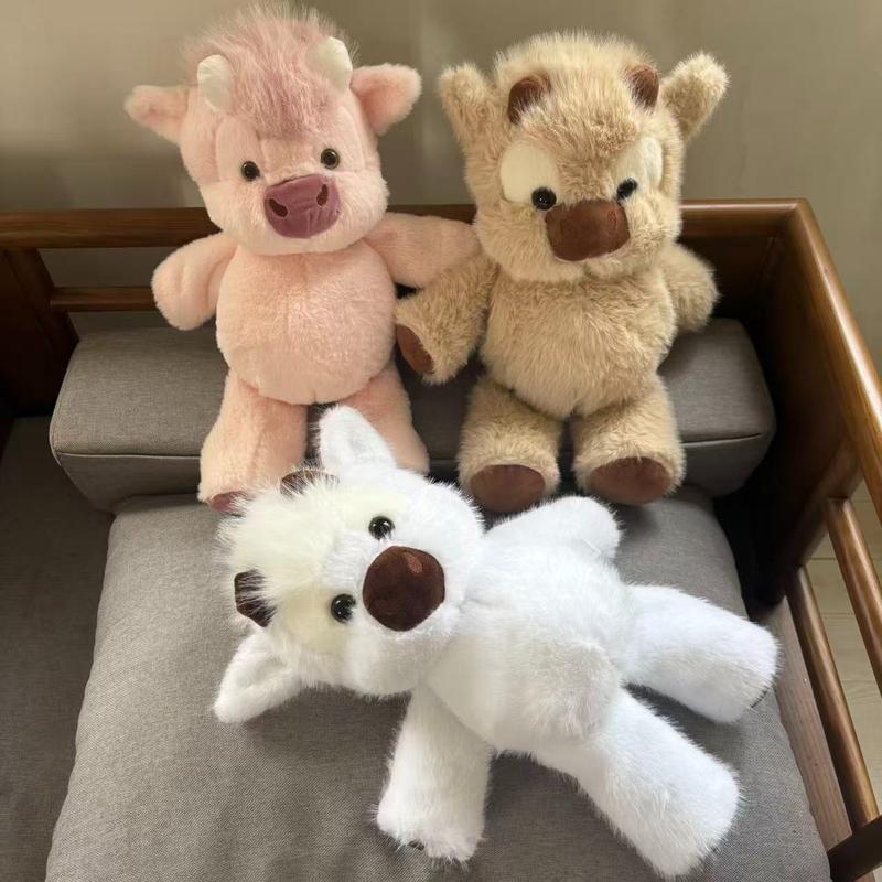 Pink, butterscotch and white Highland cow plush toys together on a sofa
