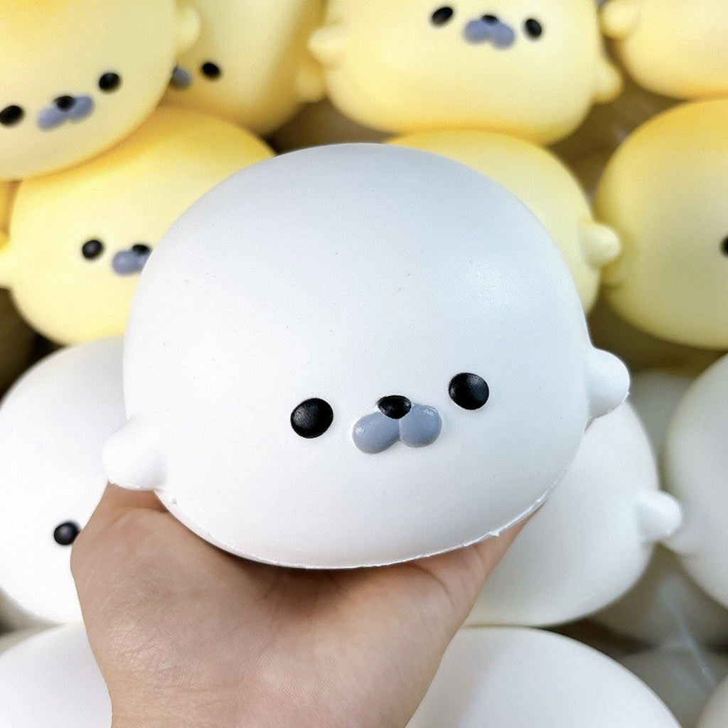 Snow white seal squishy held in one hand, with more seals behind it